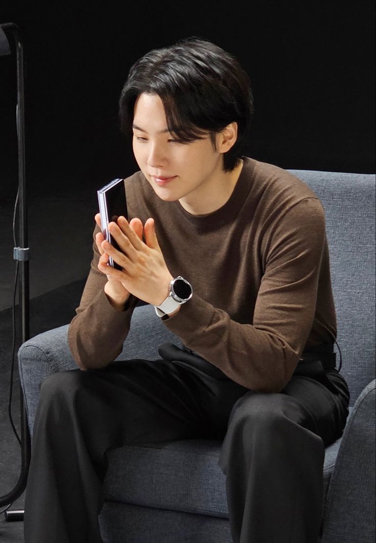 a man sitting on top of a gray couch holding a smart phone in his hands