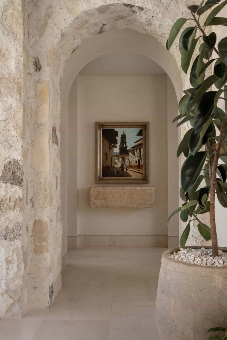 an archway leading to a bathroom with a potted plant in the corner and a painting on the wall