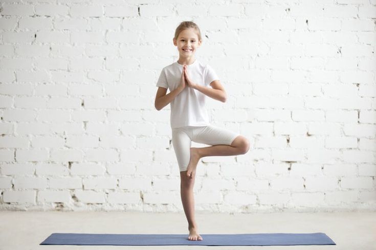 a young boy is doing yoga in front of a white brick wall and blue mat