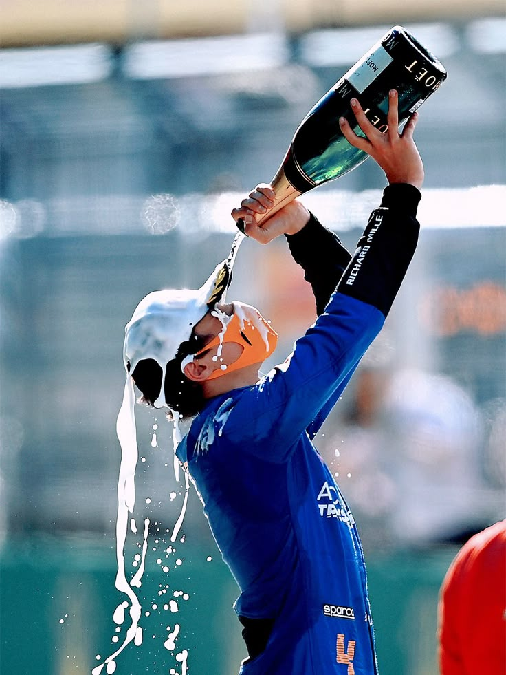 a man in blue jersey holding up a wine bottle and spraying water on his face