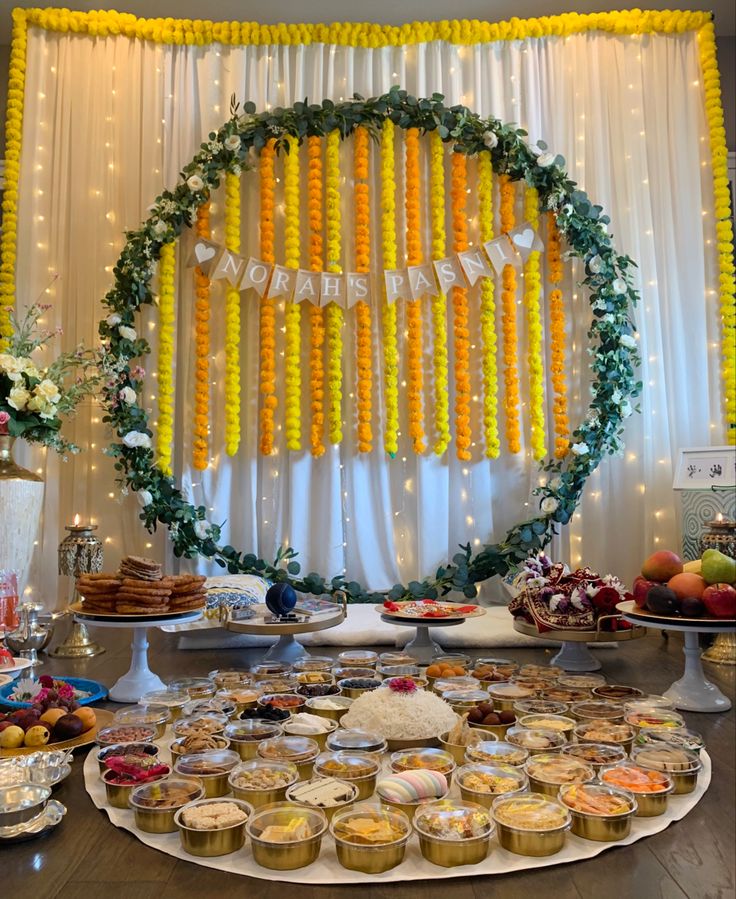 a table filled with lots of food and desserts next to a wall decorated with flowers