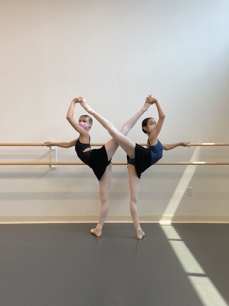 two ballerinas in black leotards are standing on one leg with their arms stretched out