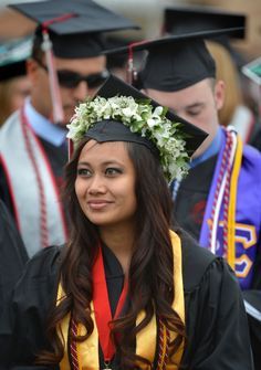 a woman wearing a graduation cap and gown with flowers in her hair is looking at the camera