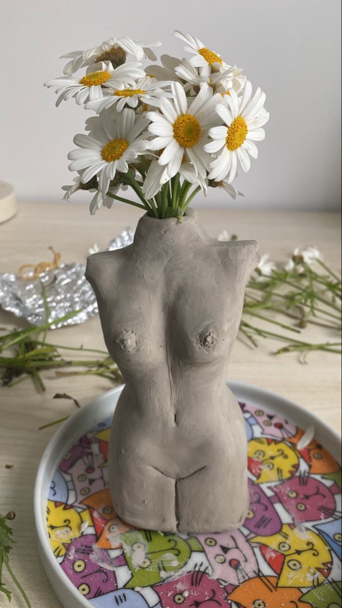 there is a vase with flowers in it on the table next to a plate that has an image of a woman's breast