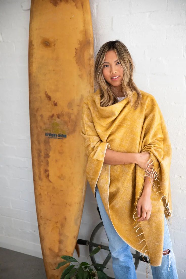 This honey-hued poncho is handwoven in Nepal on majestic wooden looms using a soft, unique yarn and finished with perfectly twisted tassels. Sewn in Western Australia, this piece is perfect for chilly mornings or cool beach evenings. It's easy to style this poncho. Wear it with the v-neck at the front or diagonal for a different look. One size fits most. Approximate size overall is 30 x 74 inches. Wash by hand in cold water and dry with care. One Size Tasseled Shawl For The Beach, Beach Shawl With Tassels, Beach Shawl With Tassels One Size, Cozy One Size Poncho For Beach, One Size Beach Shawl With Fringe, Bohemian Yellow Scarves For Beach, Beach Poncho Shawl For Fall, Cozy Fall Poncho For Beach, Bohemian Yellow Poncho One Size