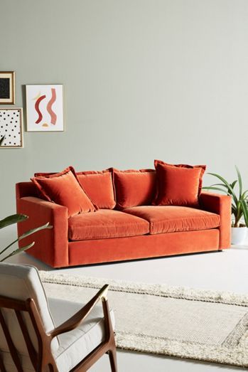 an orange couch sitting in a living room next to a chair and potted plant