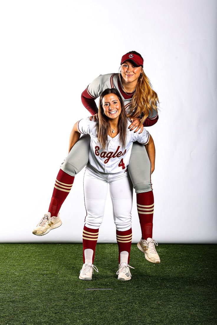 two women in baseball uniforms are posing for a photo on the field with their arms around each other