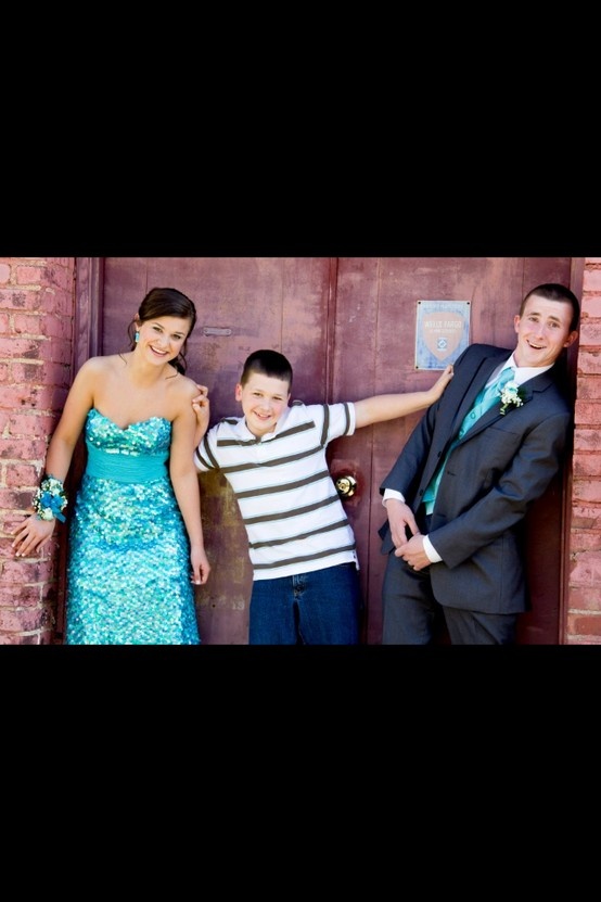 three people standing next to each other in front of a brick wall with one person wearing a suit and tie