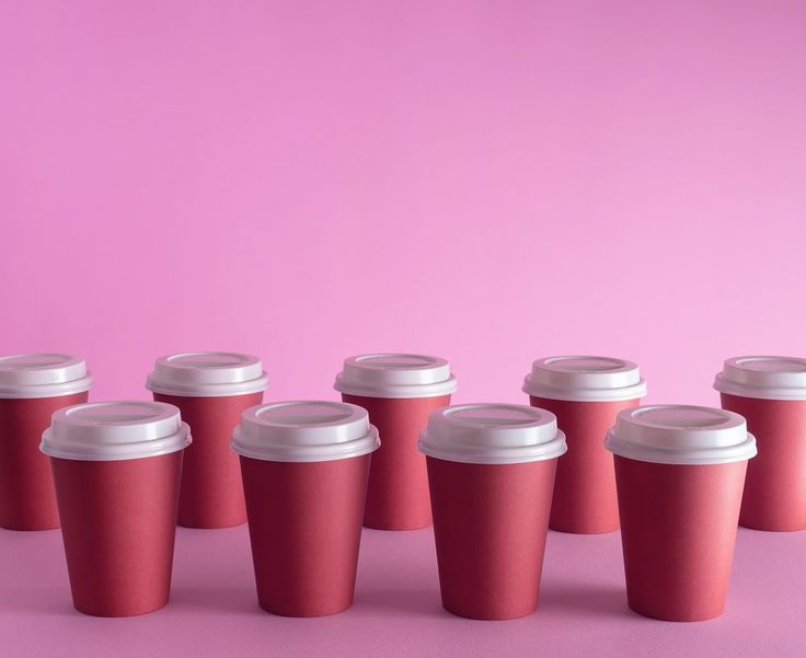 six red coffee cups lined up against a pink background with the lids slightly down on them