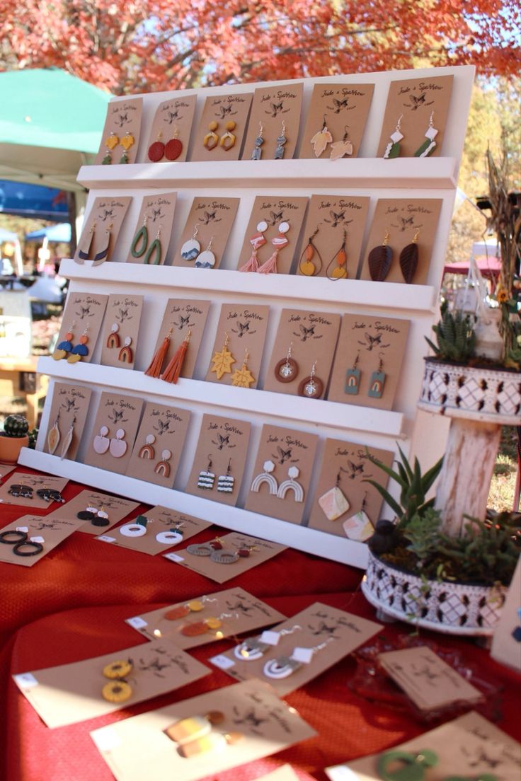 an assortment of earrings are on display at a market table in front of a tree