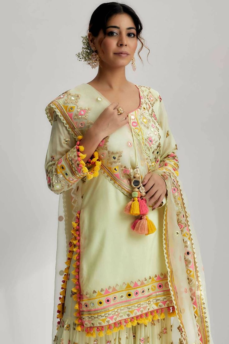 The friya short kurta sharara set with mirror work, pompoms, tassels and intricate hand and machine embroidery is a true masterpiece that celebrates artistry and craftsmanship. It is the perfect choice for festive occasions, weddings, or any special event where you want to make a lasting impression. Bohemian Semi-stitched Sharara For Festive Occasions, Pista Green Palazzo Set With Mirror Work, Bohemian Designer Dupatta With Gota Work, Bohemian Gota Work Dupatta Designer Wear, Festive Sets With Tassels And Straight Kurta, Festive Straight Kurta Sharara With Tassels, Festive Sharara With Tassels And Straight Kurta, Georgette Sets With Tassels In Traditional Drape Style, Navratri Straight Kurta Anarkali Set With Tassels