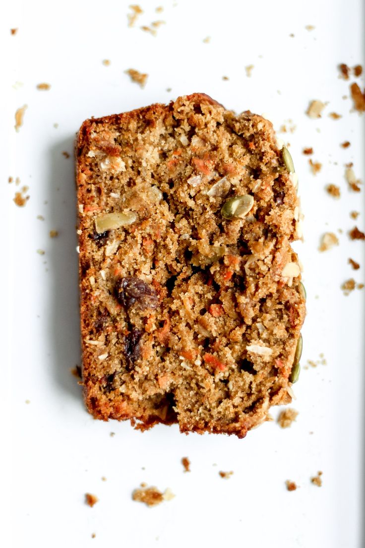 a piece of bread with nuts and seeds on it sitting on a white plate next to a fork