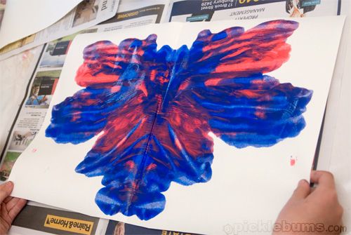 a person holding up a piece of art with blue and red paint on it,