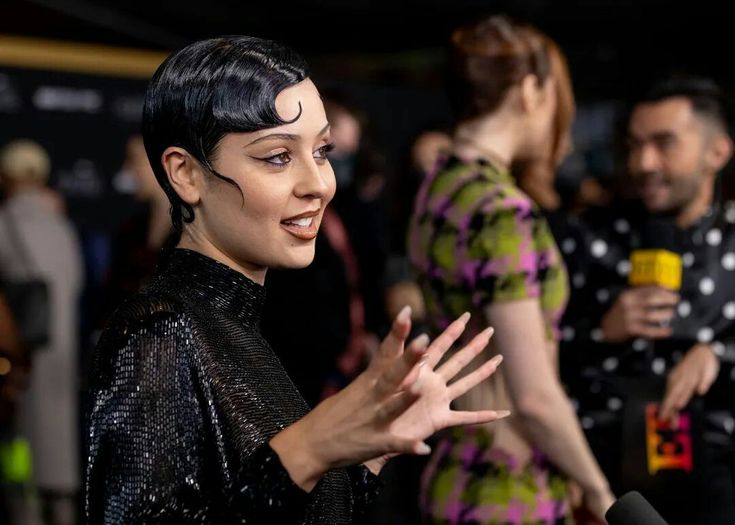 a woman with black hair and makeup talking to the media at an event stock photo