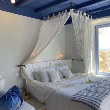 a white bed sitting under a window next to a blue painted ceiling in a bedroom