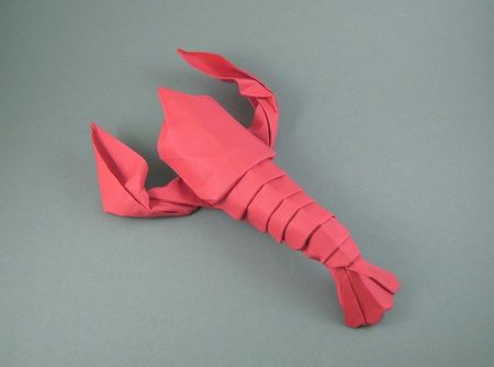 an origami crab made out of pink paper on a gray surface with the top folded up