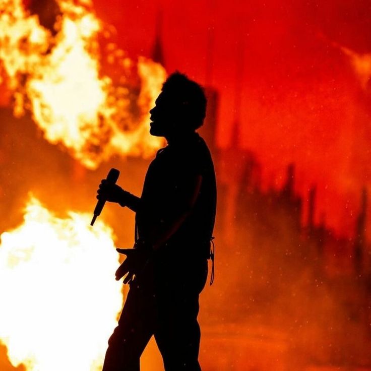 a man holding an ax in front of a fire with flames behind him and red sky