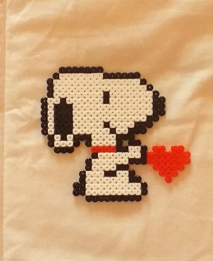 a beaded snoopy dog with a red heart on it's chest sitting next to a piece of paper