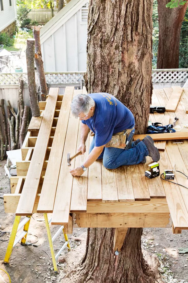 a man working on a wooden table in front of a tree with tools attached to it