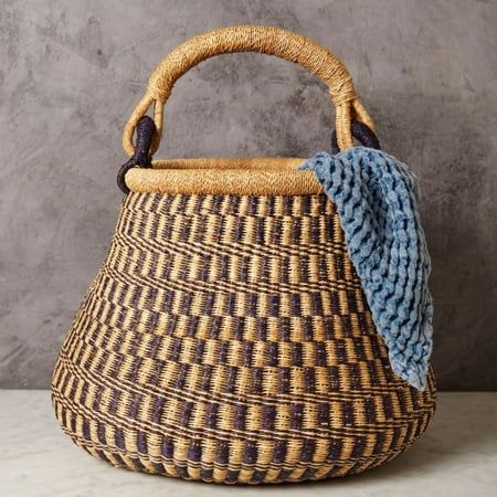 a woven basket with a blue and yellow blanket on it's handle, sitting against a gray wall