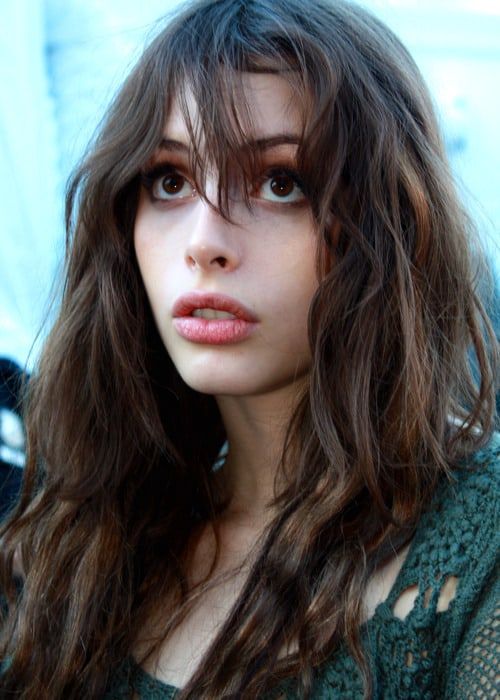 a close up of a person with long hair and wearing a green sweater looking at the camera