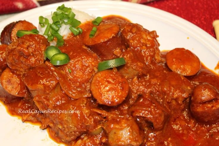 a white plate topped with meat covered in gravy and green onions on top of rice