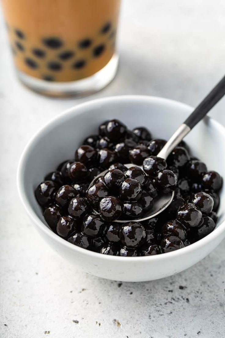 a white bowl filled with black olives next to a drink