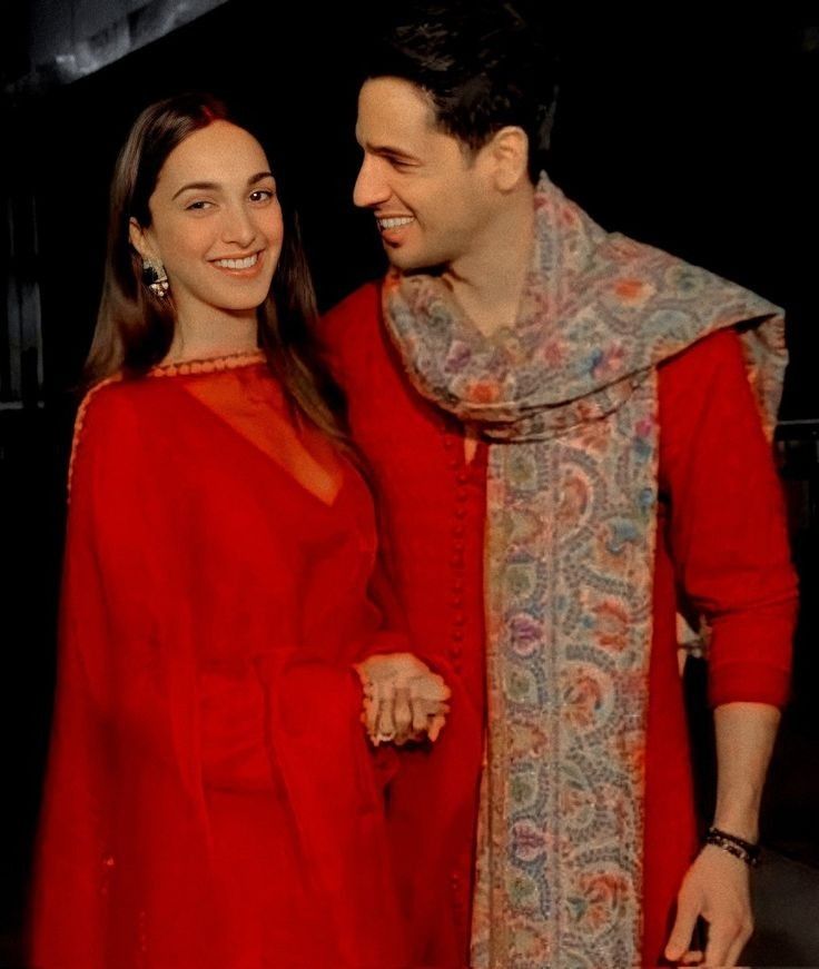 a man and woman standing next to each other in front of a black background wearing red