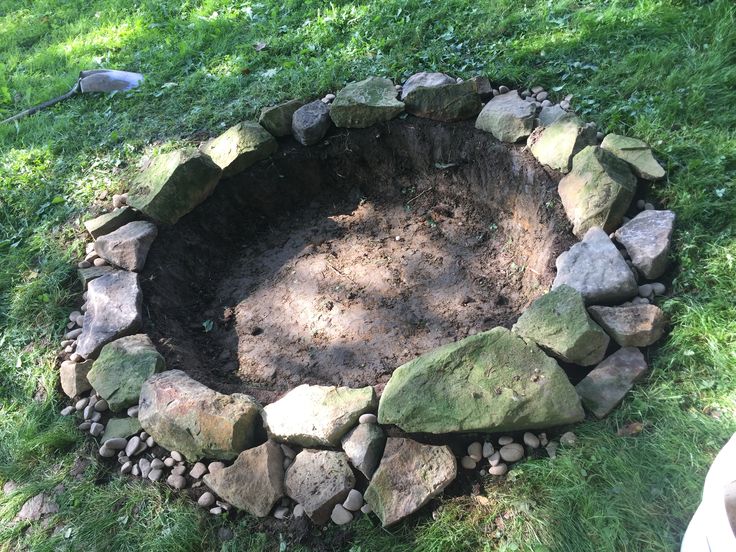 a stone fire pit in the grass with rocks around it