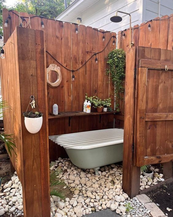 a bath tub sitting in the middle of a garden area next to a wooden fence