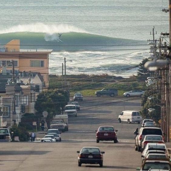 cars are parked on the side of the road as waves crash in the ocean behind them