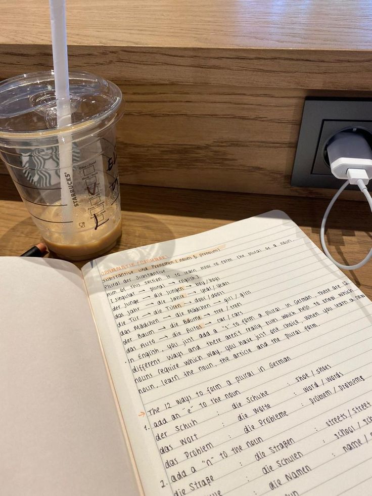 an open book sitting on top of a wooden table next to a cup of coffee