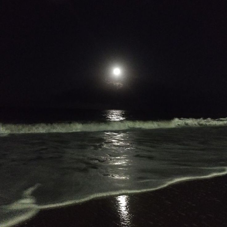 the full moon is shining over the ocean at night with waves crashing on the shore