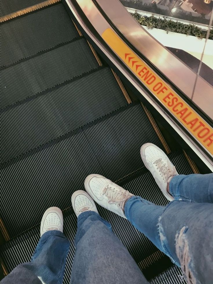 two people standing on an escalator with their feet up