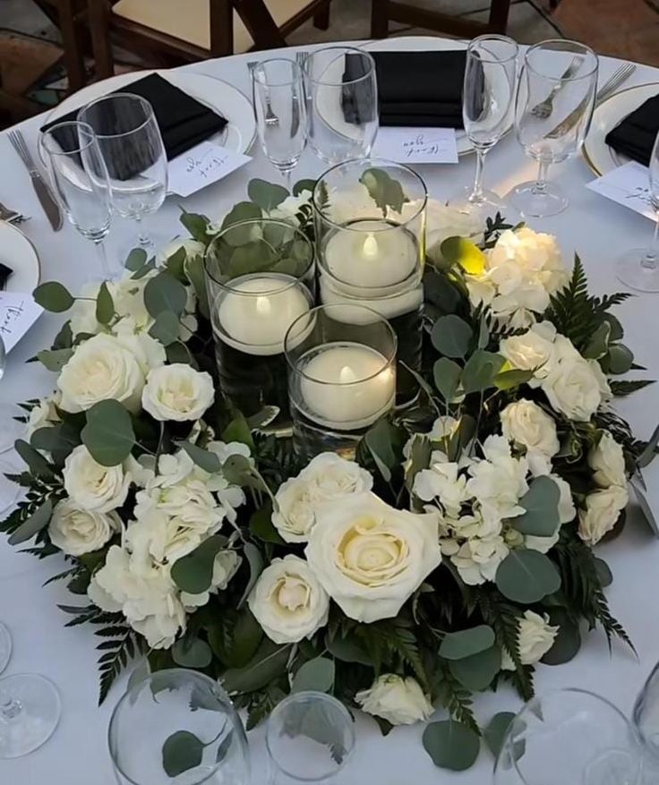 the centerpiece is made up of white roses and greenery, with candles on each side