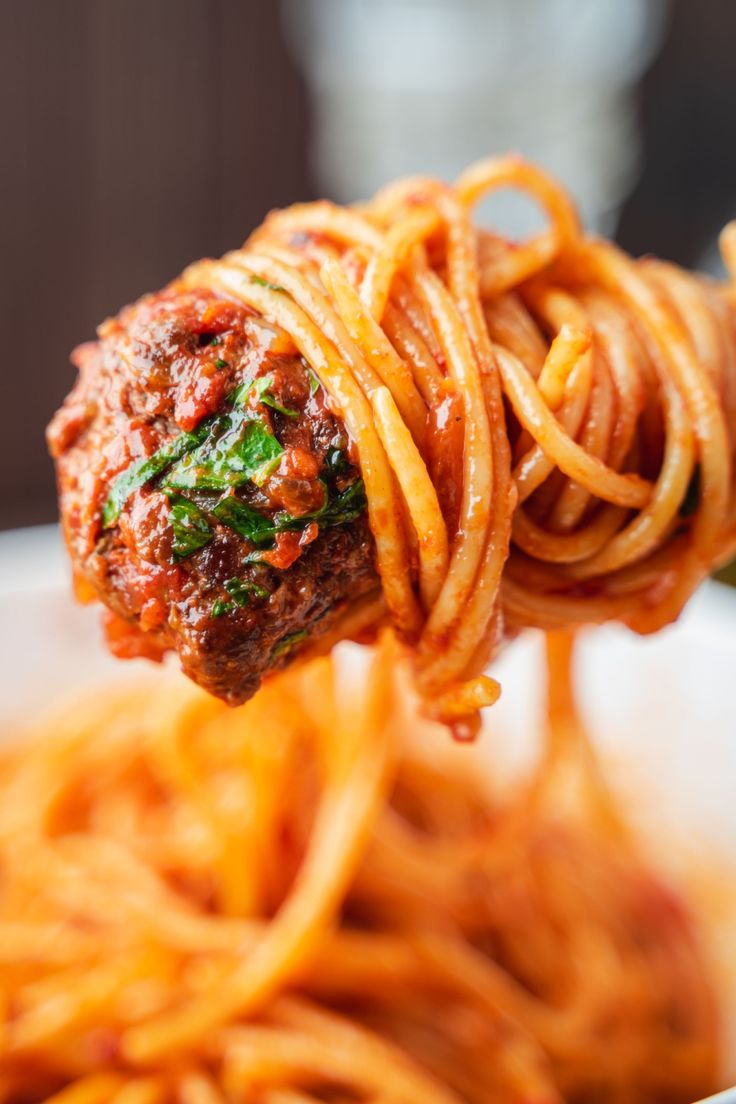 a fork full of spaghetti with meatballs and sauce on it in a white bowl