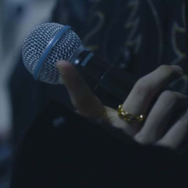 a close up of a person holding a microphone in front of a microphone mic and wearing a gold ring