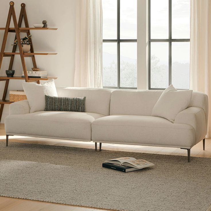 a white couch sitting in front of a window next to a book shelf with books on it