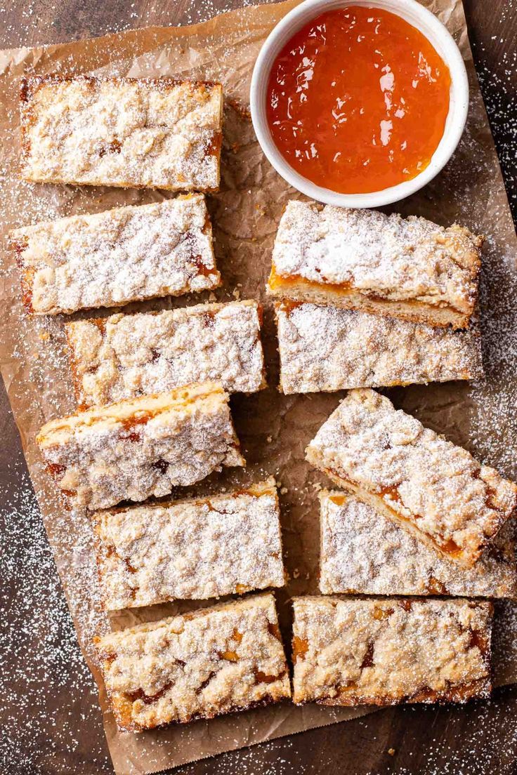 several pieces of dessert sitting on top of a cutting board next to a bowl of sauce