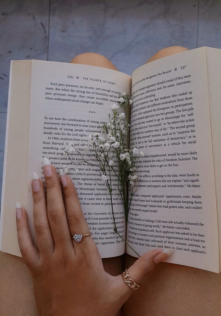 a woman is holding an open book with flowers in it and her hand on top of the book