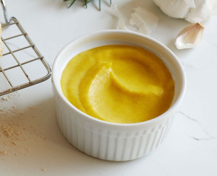 a white bowl filled with yellow sauce next to garlic