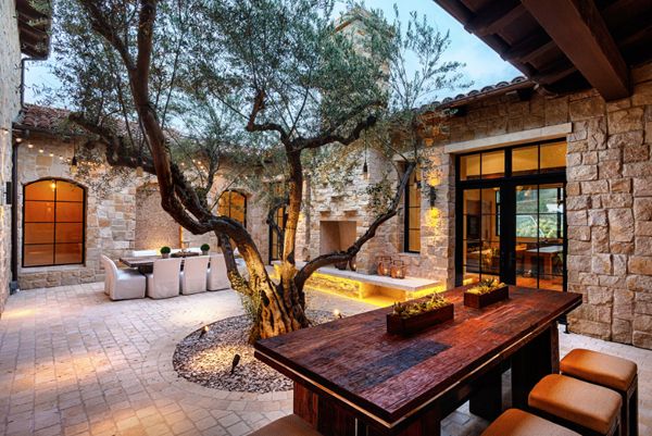 an outdoor dining area with stone walls and wooden table surrounded by brown leather chairs under a tree