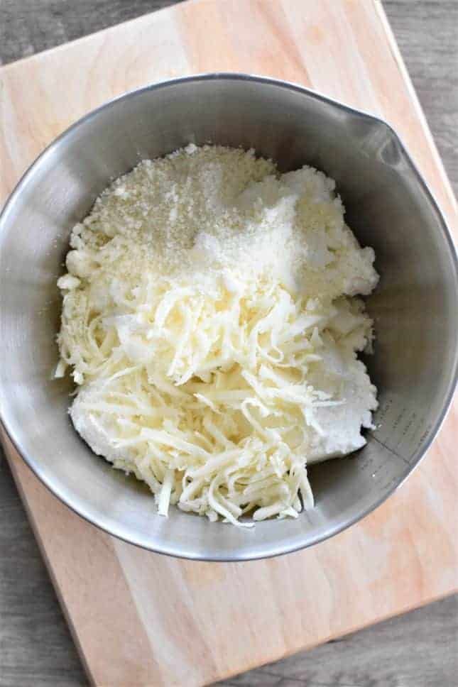 a metal bowl filled with cheese on top of a wooden cutting board