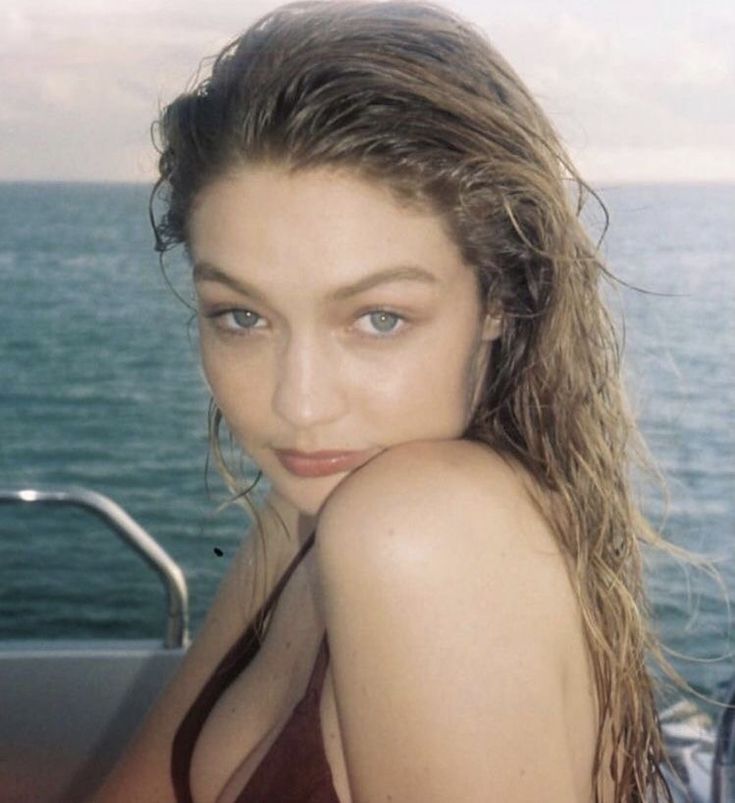 a beautiful young woman sitting on top of a boat near the ocean with her hair blowing in the wind