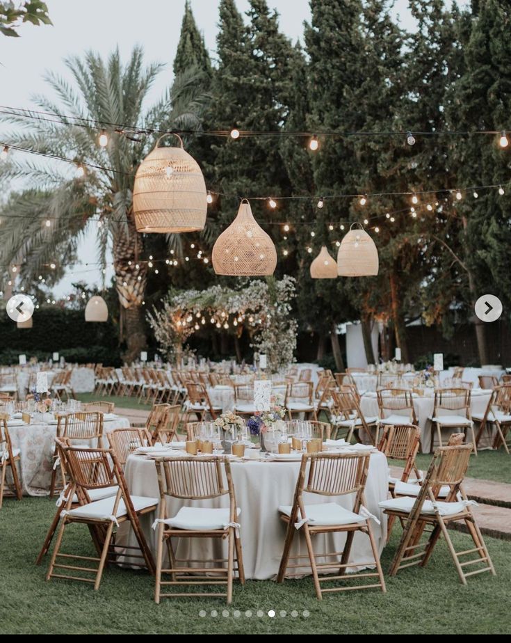 tables and chairs are set up for an outdoor wedding reception with hanging lights above them