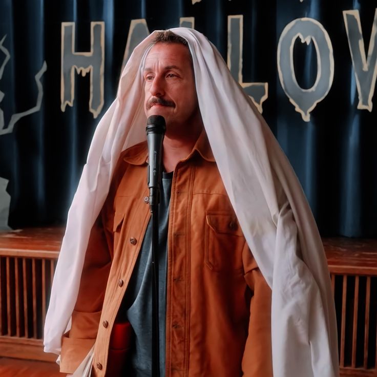 a man in an orange shirt and white veil on his head speaking into a microphone