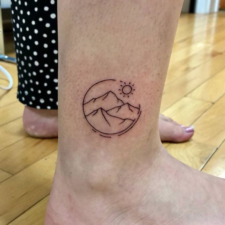 a small tattoo on the foot of a person with mountains and sun in the background