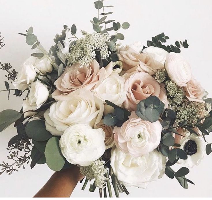 a hand holding a bouquet of white and pink flowers with greenery on the stems