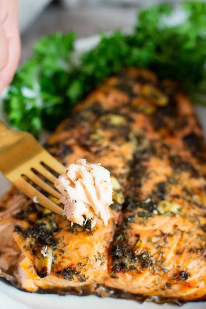 a person is holding a fork over a piece of salmon on a plate with parsley