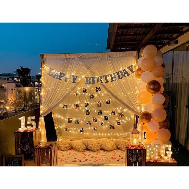 an outdoor birthday party with balloons and lights on the outside wall, decorated in gold and white